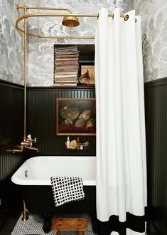 a black and white bathroom with a gold faucet, tub, bookshelf and pictures on the wall