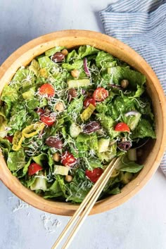 a salad in a wooden bowl with two chopsticks next to it on a table