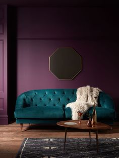 a living room with purple walls and a teal couch in the corner, next to a coffee table