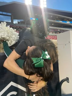 two people are hugging each other in front of a wall at a football game with the sun shining on them