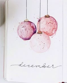 an open notebook with three ornaments hanging from it's sides and the word december written in cursive writing