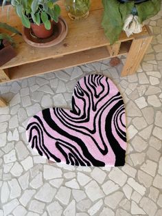 a pink and black heart shaped rug sitting on top of a wooden bench next to potted plants