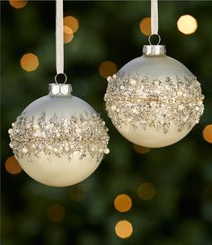 two white ornaments hanging from a christmas tree with lights in the back ground behind them