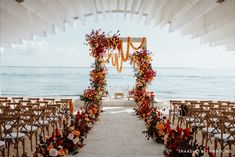 an outdoor ceremony set up on the beach with orange and red flowers, greenery and candles