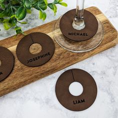 three coasters with names on them sitting next to a glass and potted plant