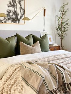 a bed with pillows and blankets on top of it next to a painting above the headboard