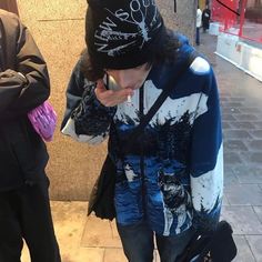 a man with a cell phone standing next to a building while wearing a beanie