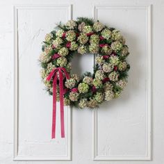 a wreath hanging on the front door of a house with pink ribbon and bow around it