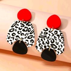 two pairs of leopard print and red earrings hanging from a hook on a pink wall