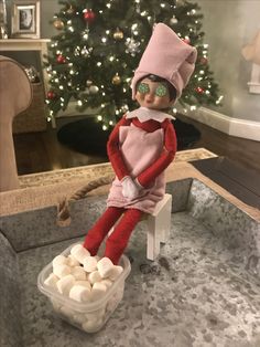 an elf sitting on a chair with marshmallows in front of a christmas tree