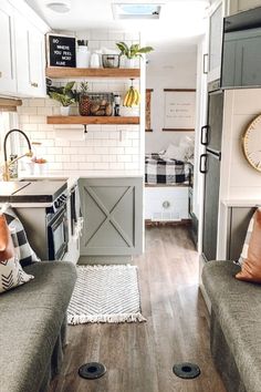 the interior of a tiny home with wood floors and gray couches, white cabinets, and open shelving