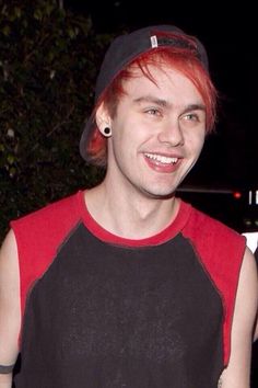 a young man with red hair wearing a black and red baseball cap smiles at the camera