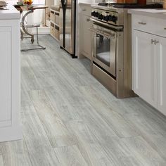 a kitchen with white cabinets and wood flooring, an oven in the center is surrounded by stainless steel appliances