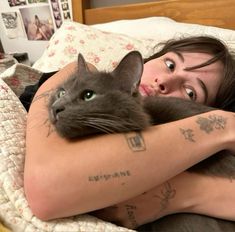 a woman laying in bed with her arm wrapped around a cat and looking at the camera