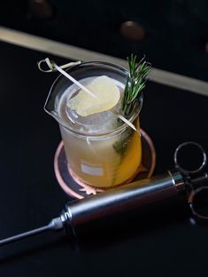 a cocktail with rosemary garnish in a glass next to a pair of scissors