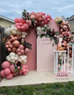 a pink and white backdrop with balloons, flowers and greenery on the side of it