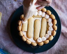 a person decorating a cake with marshmallows and cookies on the top