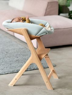 a baby laying in a wooden highchair on the floor next to a couch