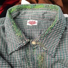 a green and white checkered shirt sitting on top of a wooden table next to other clothing