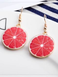 a pair of pink grapefruit earrings sitting on top of a white plate