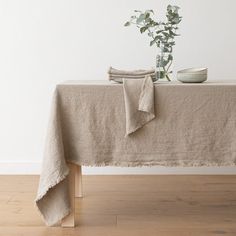 a table topped with a white vase filled with flowers next to a cloth covered table