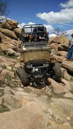 a jeep driving on rocks with people in the back ground looking at something behind it