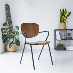 a wooden chair sitting next to a potted plant in a room with white walls