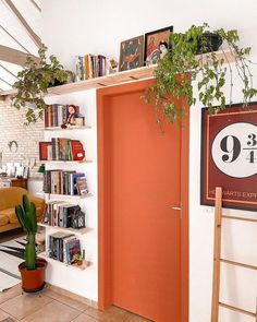 an orange door in a white room next to a book shelf with books on it