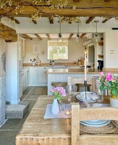 a dining room table with flowers in vases on top of it and an open kitchen area