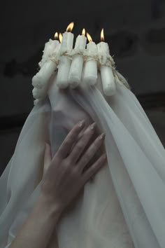 a woman's hands are wrapped in white fabric with candles sticking out of them