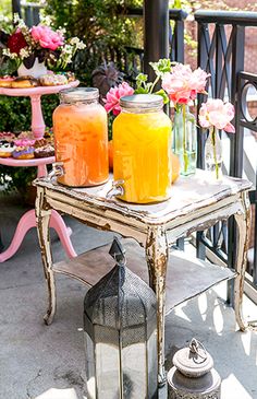 two mason jars filled with orange juice sit on a small table next to a potted plant