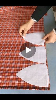 someone is cutting fabric with scissors on top of a plaid table cloth that has been folded