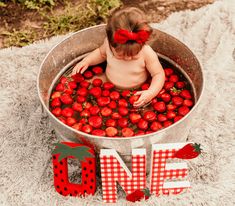 a baby sitting in a metal tub filled with strawberries next to the word love