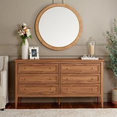 a wooden dresser sitting next to a white chair and a round mirror on the wall