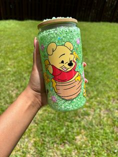 a person holding up a cup with a cartoon bear on it in the grass outside