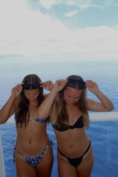 two women in bikinis standing next to each other on a boat near the ocean