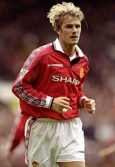 a man with blonde hair wearing a red shirt and white shorts on a soccer field