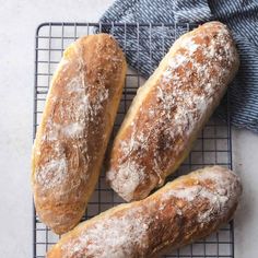 three loaves of bread sitting on top of a cooling rack next to a blue towel