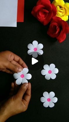 someone is cutting out paper flowers on a black surface with red, white and yellow roses