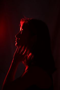 a woman in the dark with her hand on her face and red light behind her