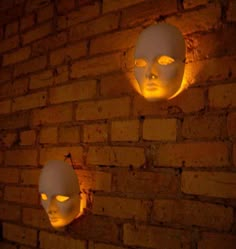 two white masks with glowing eyes are on the brick wall in front of a light