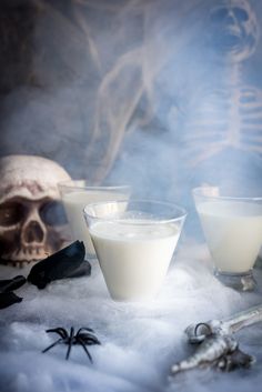 two glasses filled with liquid sitting on top of snow next to a skull and bones