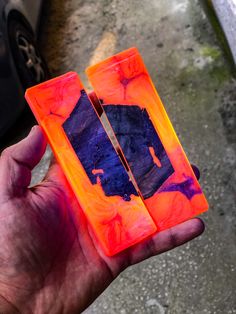 two orange and purple pieces of glass held in someone's hand with a car behind them