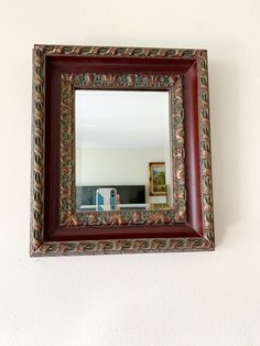 a mirror is hanging on the wall above a shelf with a vase and other items