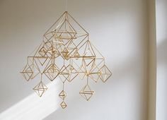 a gold sculpture hanging from the side of a white wall next to a window with sunlight streaming through it