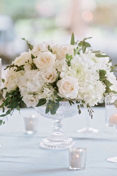 a centerpiece with white flowers and greenery on a table