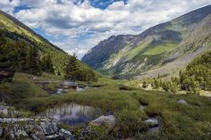 there is a small pond in the middle of this mountain valley with mountains in the background