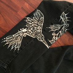 a pair of black jeans with an embroidered bird on the front and side, sitting on top of a wooden floor