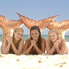 three beautiful young women laying on top of a sandy beach