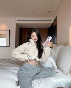 a young woman sitting on top of a bed holding a cell phone in her hand